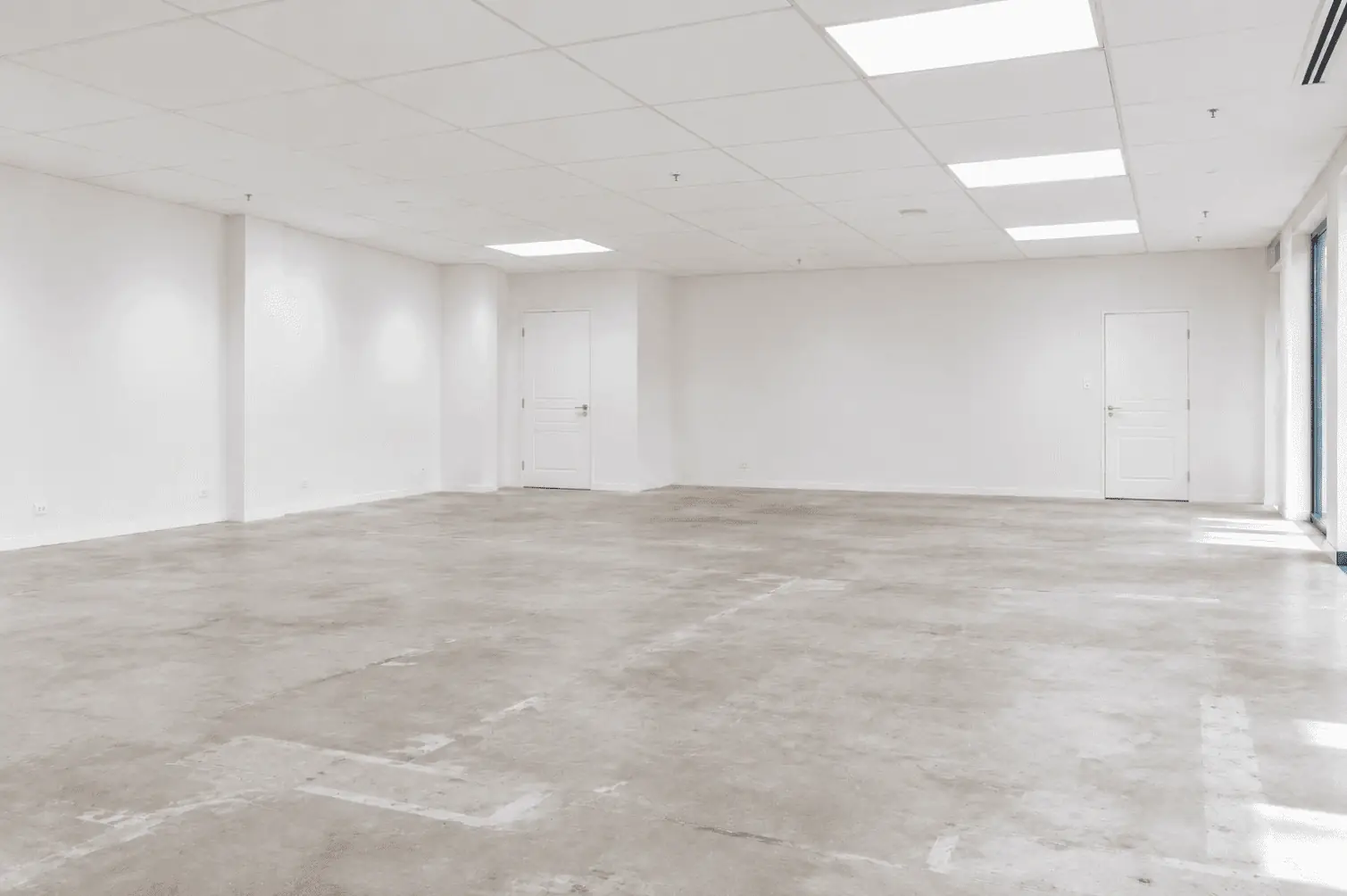 An empty office tenancy after make good: white walls, a clean ceiling grid with light panels and a bare concrete floor, ready to hand back