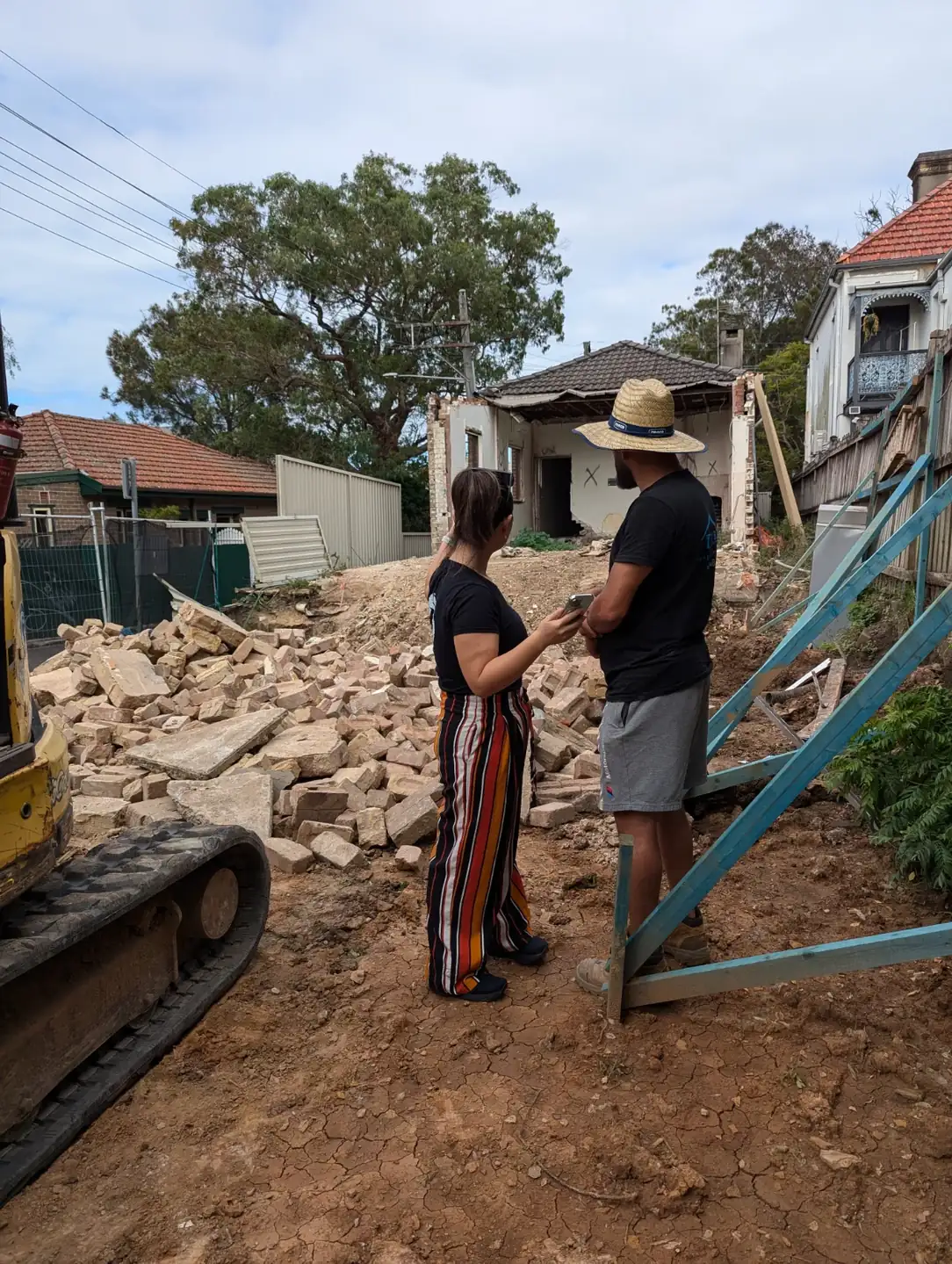 An OIC architect and a builder talking beside the rubble of a part-demolished house
