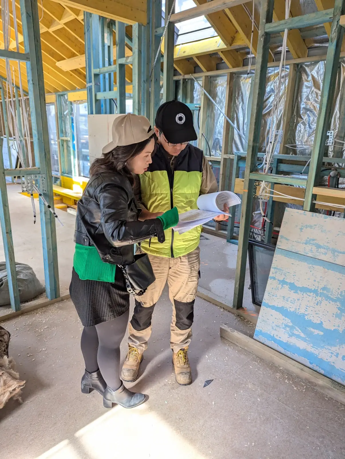 An OIC architect and a builder reading a document together inside a newly framed house