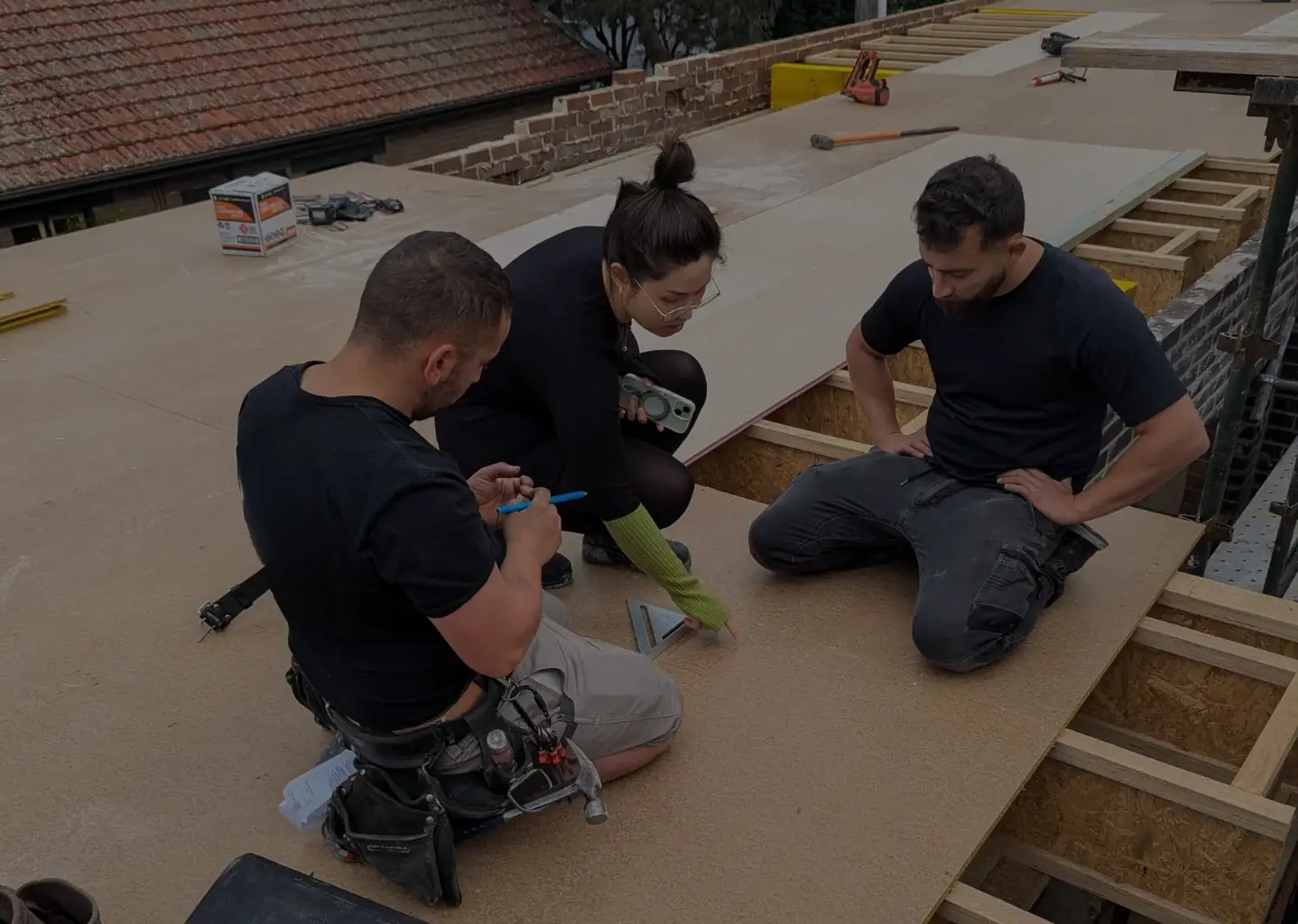 An OIC team member and two builders kneeling on a new floor deck, checking measurements together