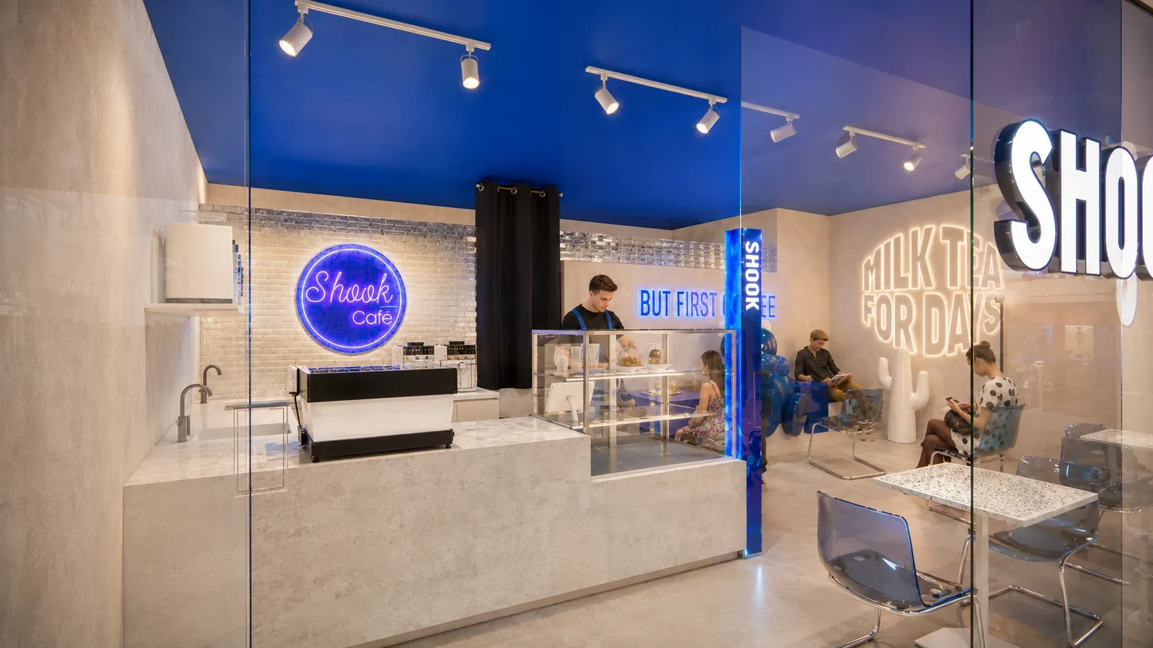 The café seen through its glass front: a blue ceiling, neon signs and stone tables, Shook Cafe, Waterloo