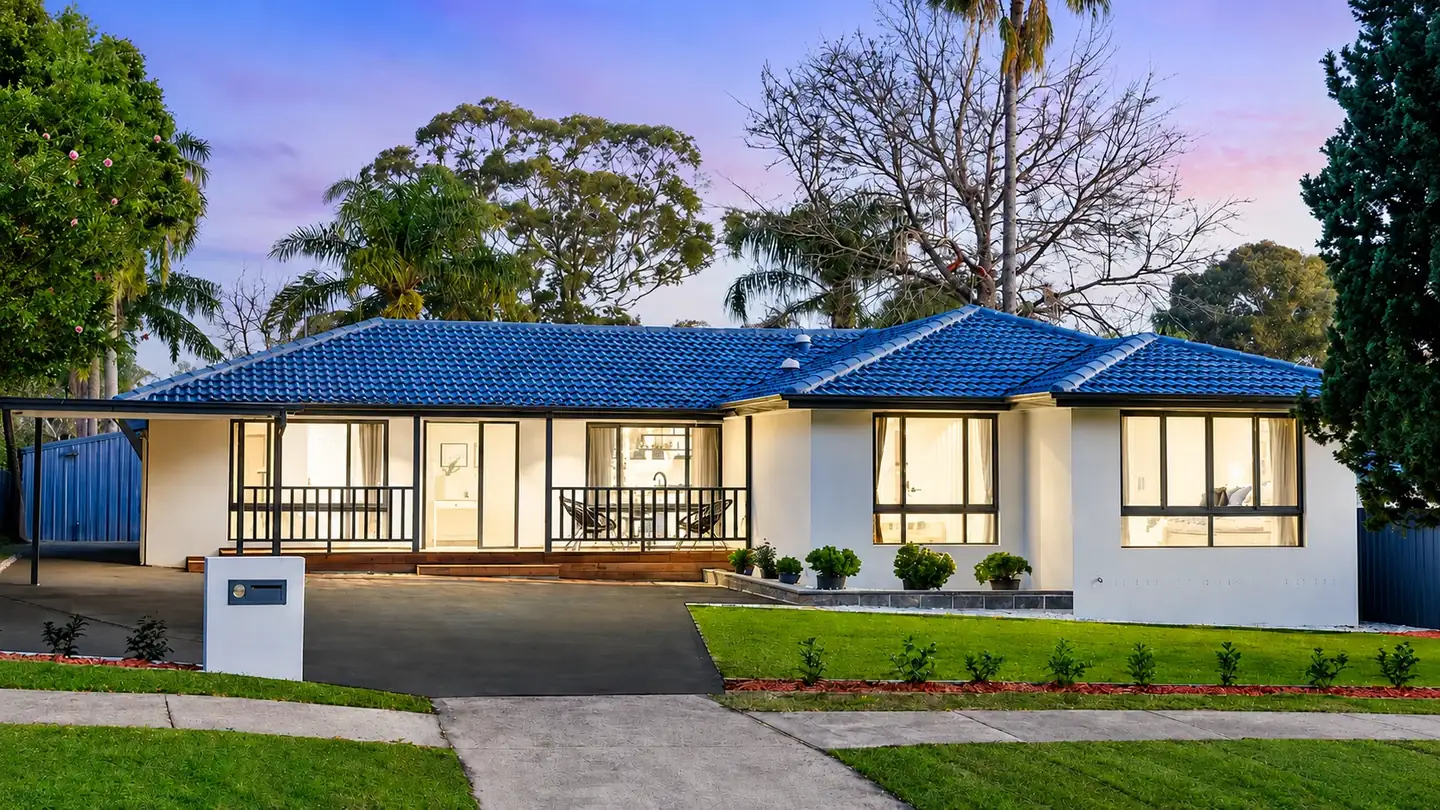The Residence in Baulkham Hills at dusk: a single-storey home with a blue tiled roof and lit windows behind a lawn